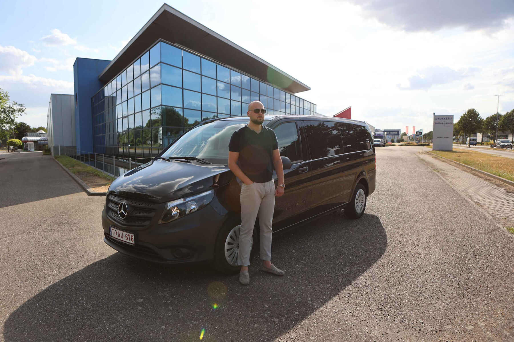 Sander naast zijn zwarte Mercedes Vito voor een modern kantoorgebouw